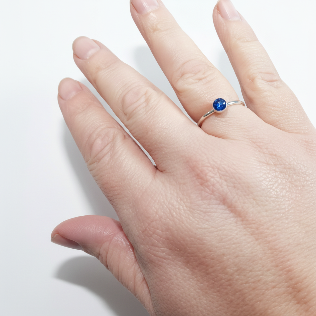 Hand wearing an ashes memorial ring with a blue gemstone