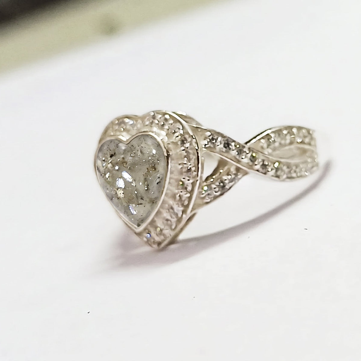 A silver heart-shaped ashes memorial ring featuring a clear heart ashes stone surrounded by cubic zirconia on a white background.