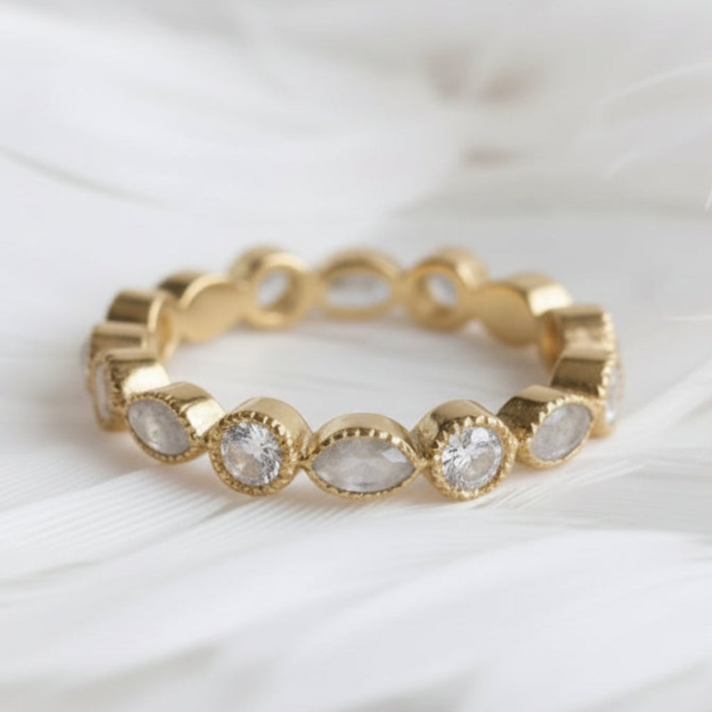 A gold ashes eternity ring featuring clear natural ashes stones and round natural diamonds, displayed on a soft white feather background.