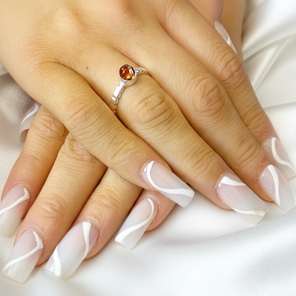 Close-up of a hand with a silver ring featuring an amber ashes memorial stone on a white fabric background.