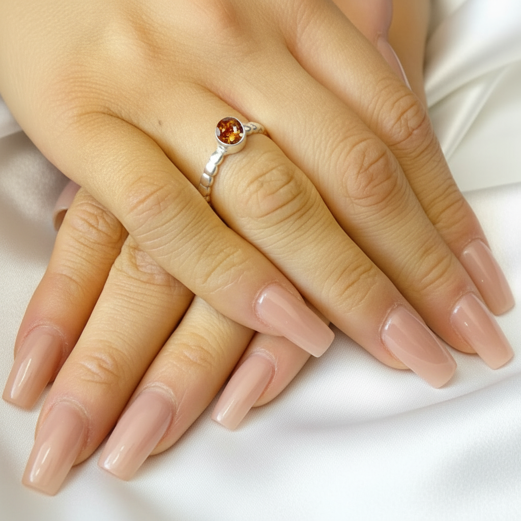 Close-up of a hand with a silver ring featuring an amber ashes memorial stone on a white fabric background.
