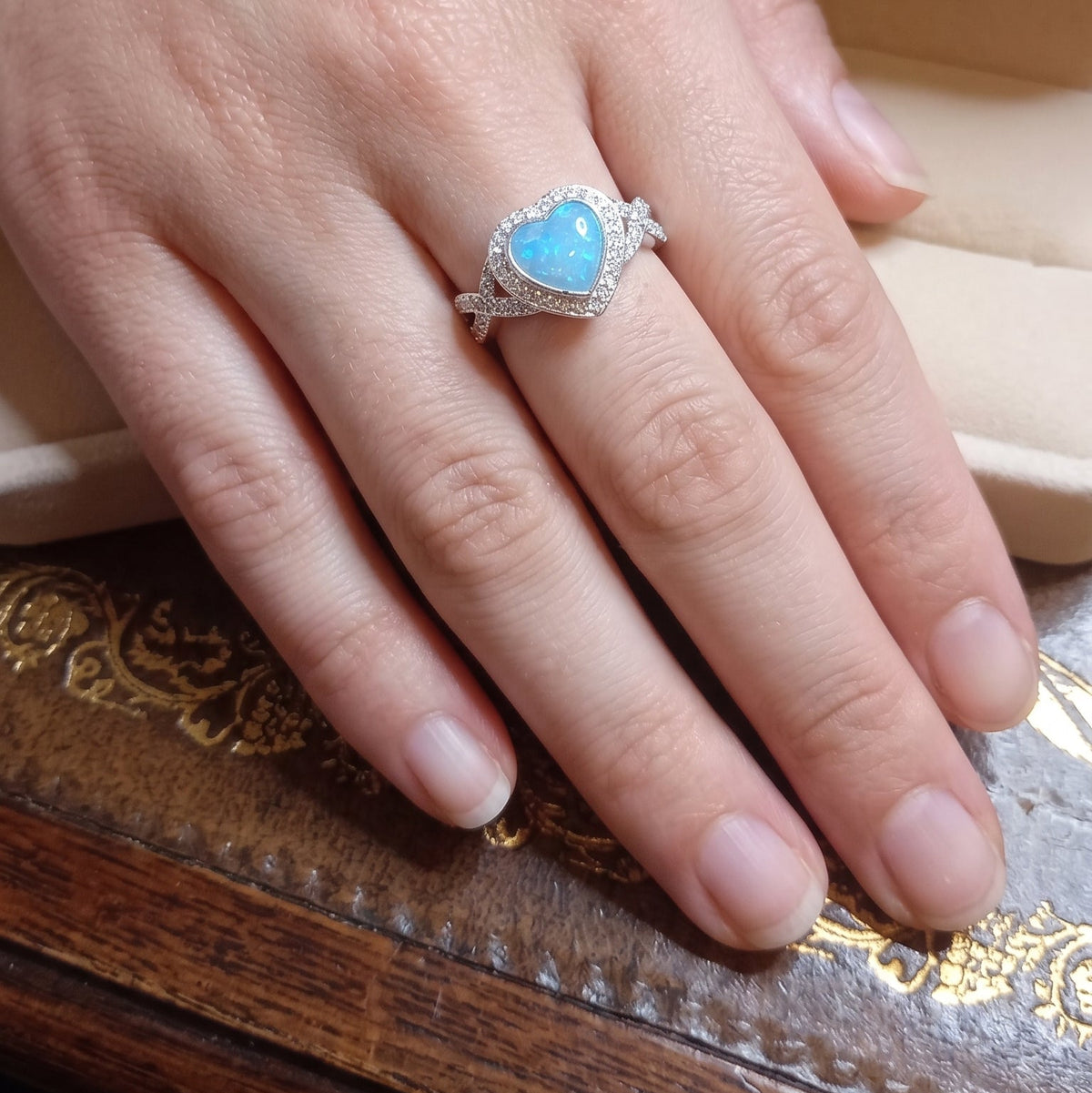 blue opal ashes memorial ring in a heart shaped central stone with a halo of cubic zirconia and crossover shoulders. on a models hand
