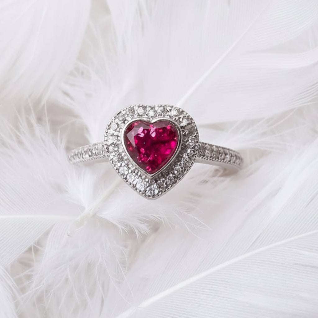 sterling silver heart halo cremation ashes memorial ring, with ruby ashes heart shaped stone, and a halo of cubic zirconia.  On background of white feathers