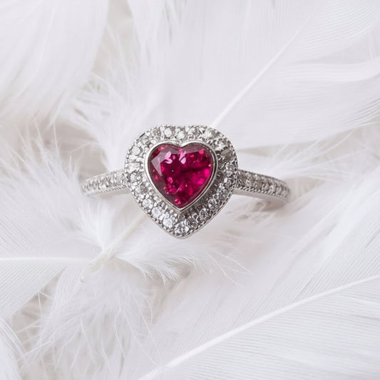 sterling silver heart halo cremation ashes memorial ring, with ruby ashes heart shaped stone, and a halo of cubic zirconia.  On background of white feathers