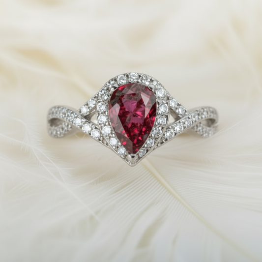 Silver crossover teardrop ring with a red ashes memorial stone on feather background