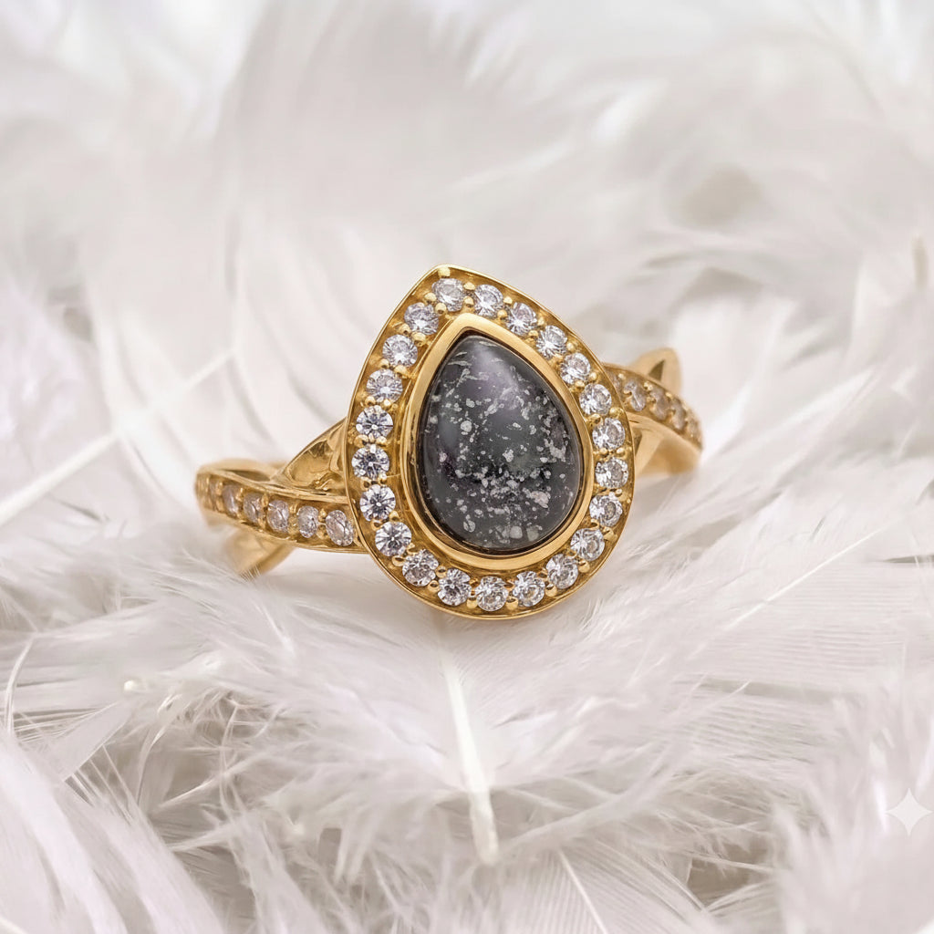 14ct gold ashes memorial halo ring with a teardrop-shaped black pearl ashes stones, accented with real diamonds, resting on white feathers.