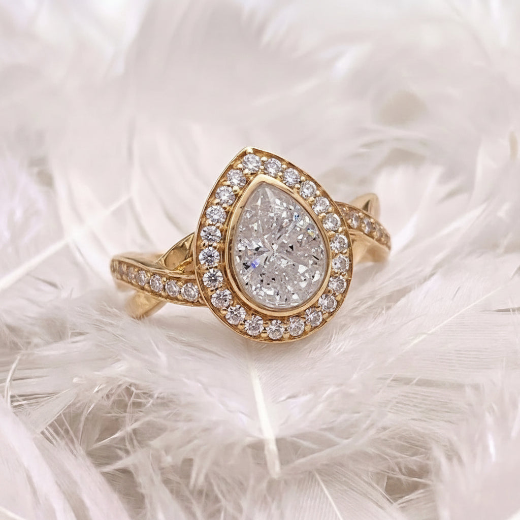 A teardrop-shaped  ashes memorial ring set with genuine diamonds with a halo and pavé band, resting on white feathers.