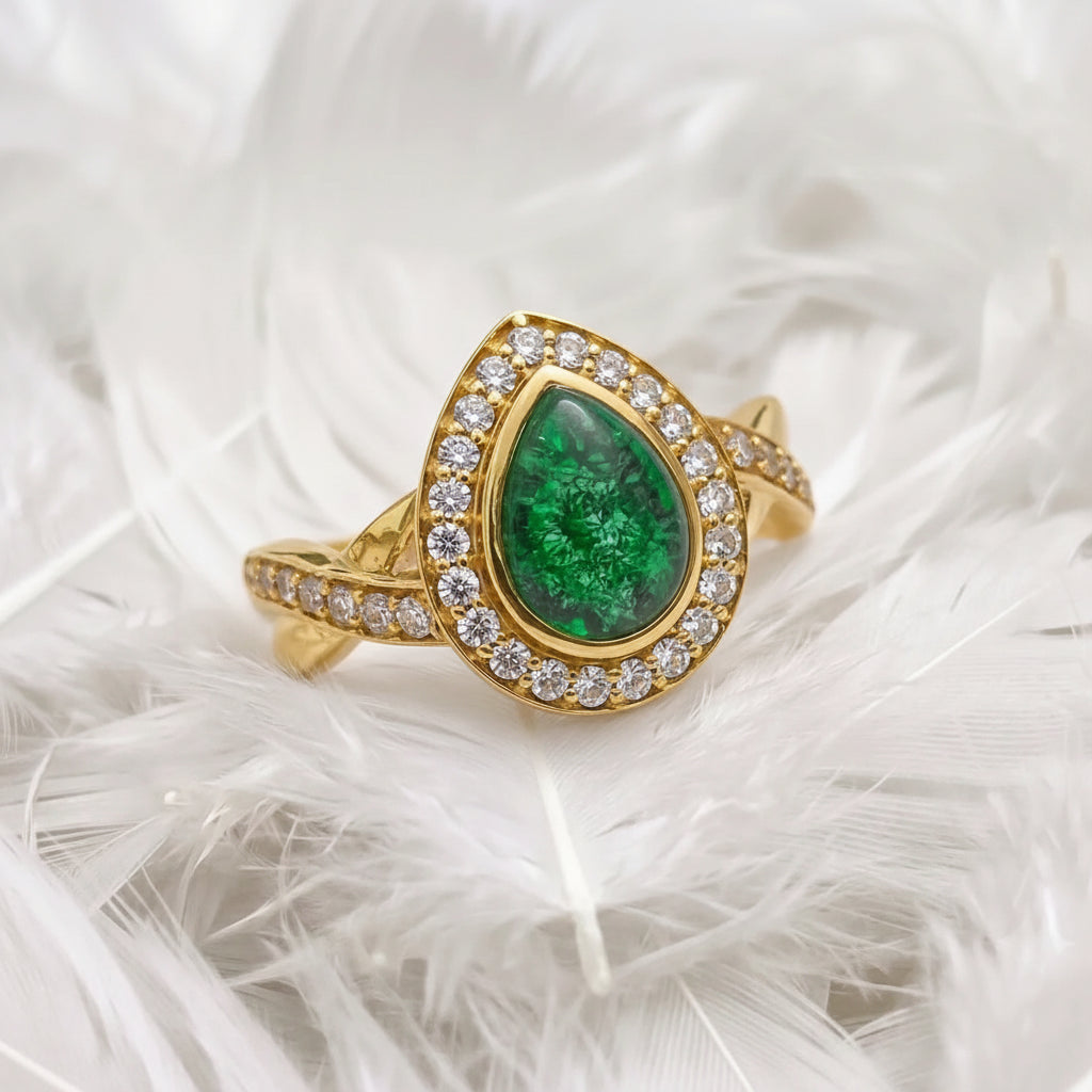 A teardrop-shaped ashes memorial ring featuring emerald pear ashes stone, surrounded by a halo of genuine diamonds, pavé-set accents, resting on white feathers.