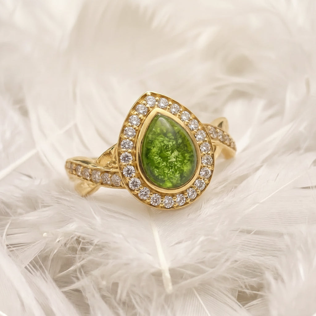 14ct or 18ct gold ashes memorial teardrop-shaped ring featuring a peridot ashes stone in the centre, surrounded by a halo of real diamonds, resting on a bed of white feathers.