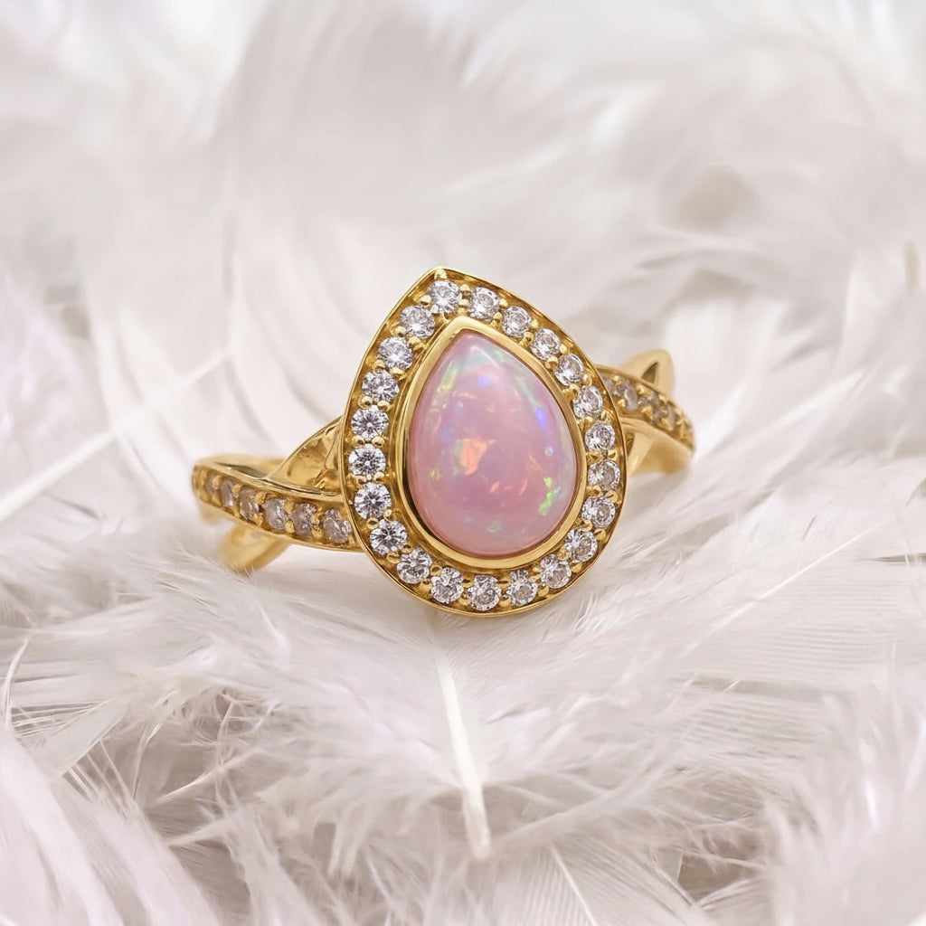 14ct gold ashes memorial teardrop ring featuring a pink iridescent opal ashes stone surrounded by a halo of real diamonds, displayed on soft white feathers.
