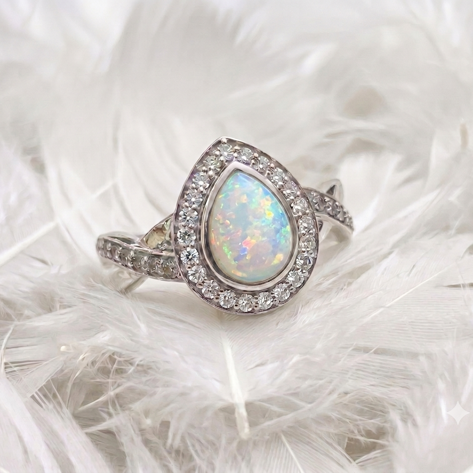 silver pear shaped ashes memorial ring set with opal and featuring crossover twist to shoulders. white feather background