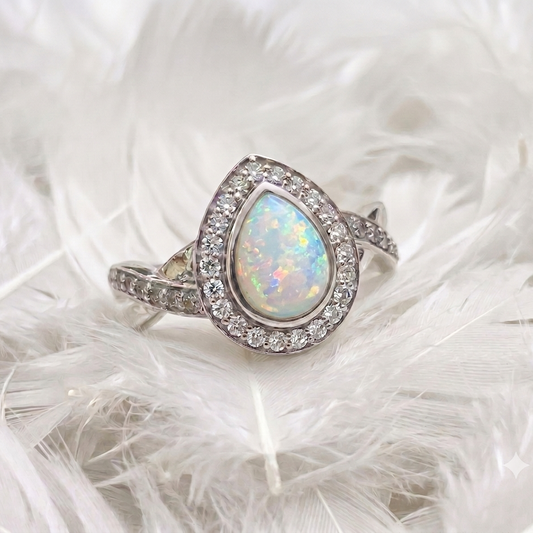 silver pear shaped ashes memorial ring set with opal and featuring crossover twist to shoulders. white feather background
