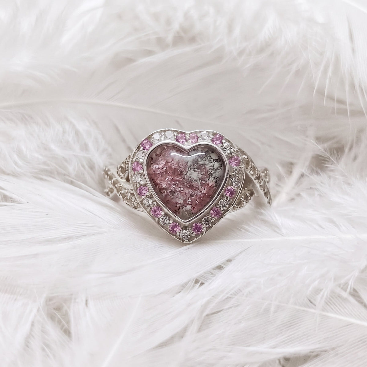 pink heart shaped memorial ashes ring with a halo of alternating pink and white cubic zirconia stones, and a crossover features on the shoulders.