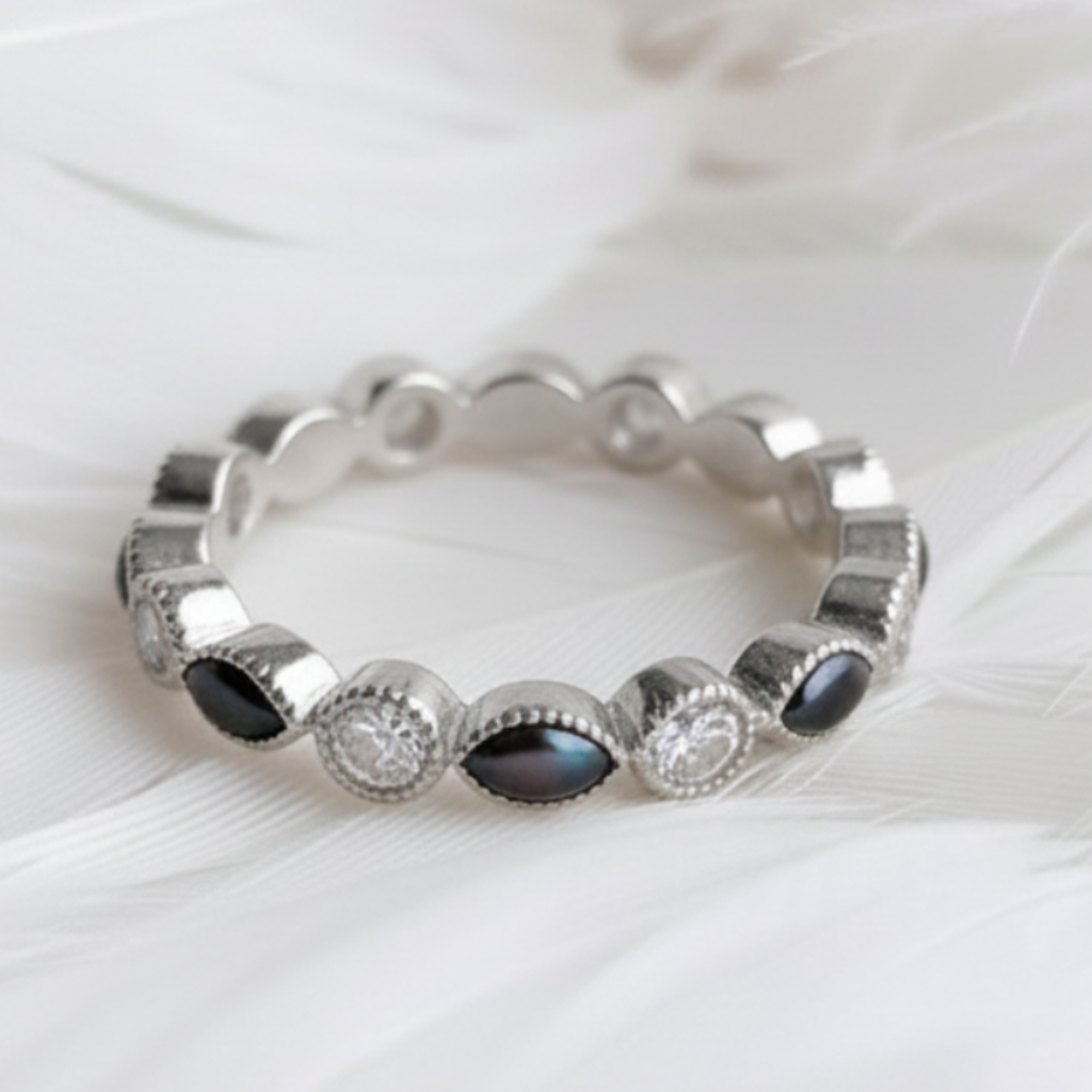 A silver ashes eternity ring featuring black pearl marquis ashes stones, and cubic zirconia round stones, displayed on a soft white feather background.