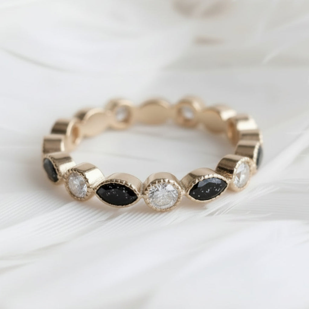 A gold ashes eternity ring featuring alternating oval black onyx ashes stones and dsiamonds, displayed on a soft white feather background.