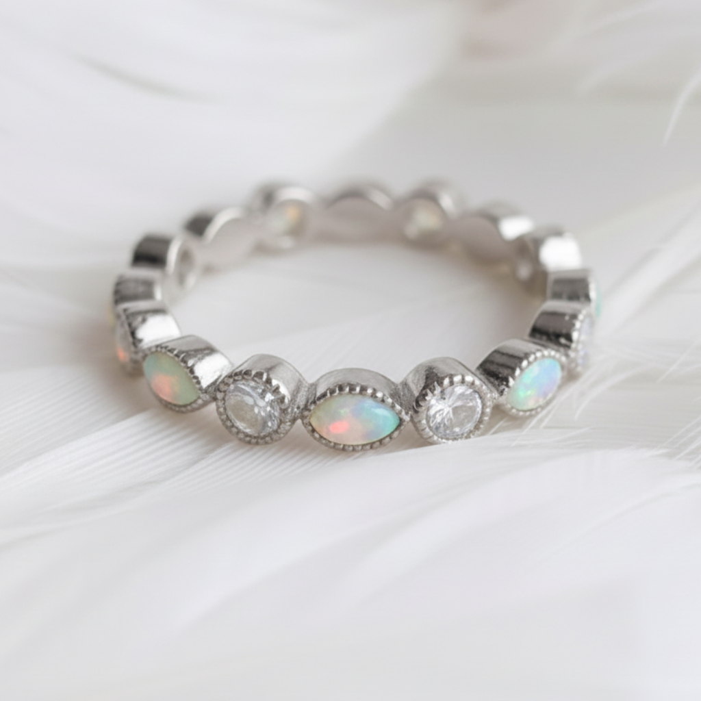 A silver eternity ashes ring featuring white opal ashes stones and clear round cubic zirconia stones, displayed on a soft white feather background.