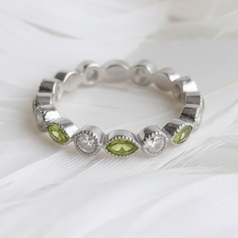 A silver eternity ashes ring featuring peridot ashes stones displayed on a soft white feather background.
