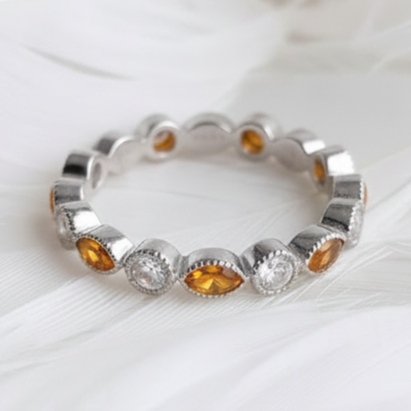 A silver ashes eternity ring featuring marquis amber ashes stones, displayed on a soft white feather background.