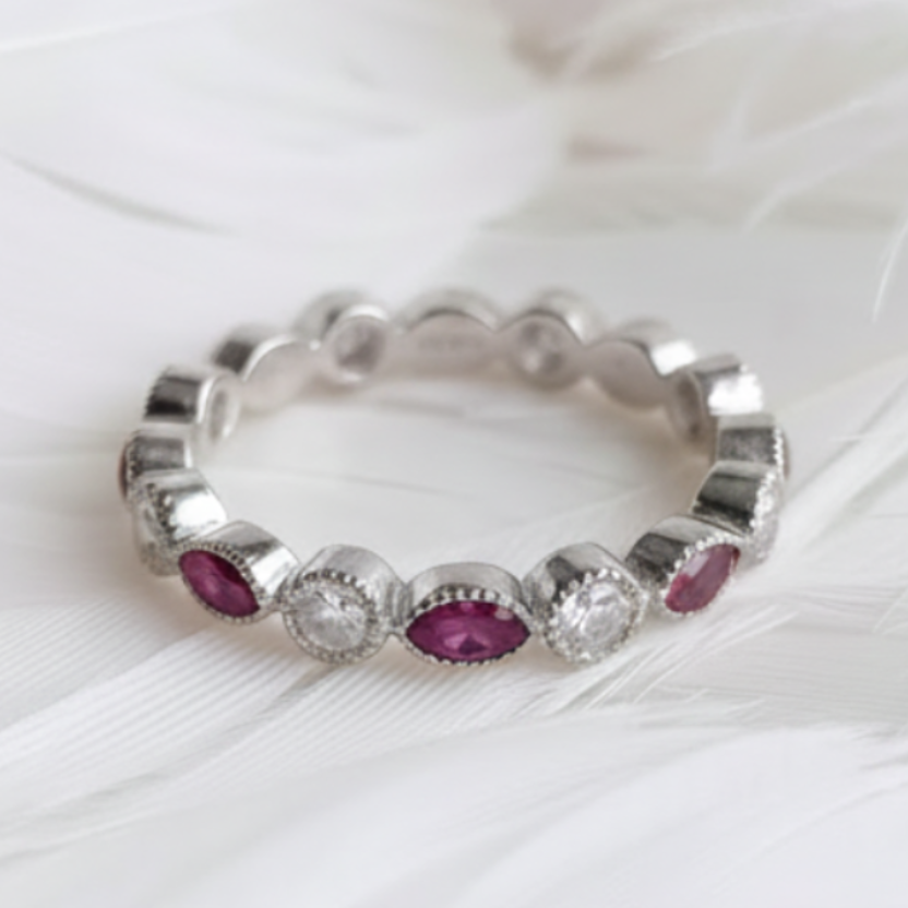 A silver ashes eternity ring featuring marquis amethyst ashes stones on a soft white feather background.