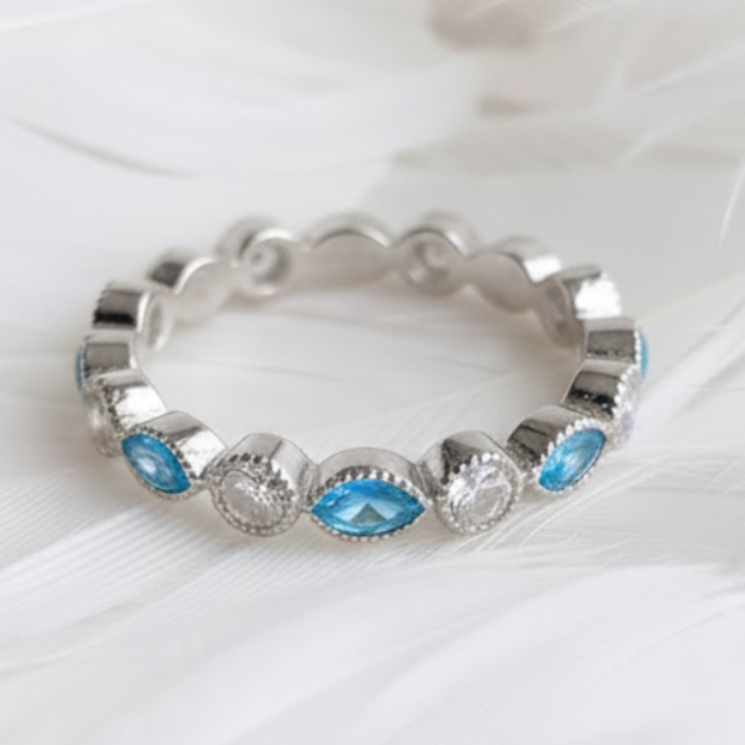 A silver eternity ashes  ring featuring marquis blue topaz ashes stones displayed on a soft white feather background.