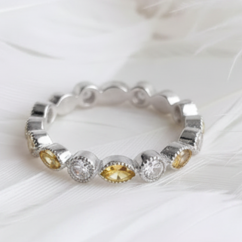 A silver eternity ashes ring featuring citrine marquis ashes stones, displayed on a soft white feather background.