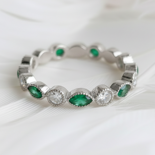 A silver ashes eternity ring featuring marquis emerald ashes stones and clear cubic zirconia stones, displayed on a soft white feather background.