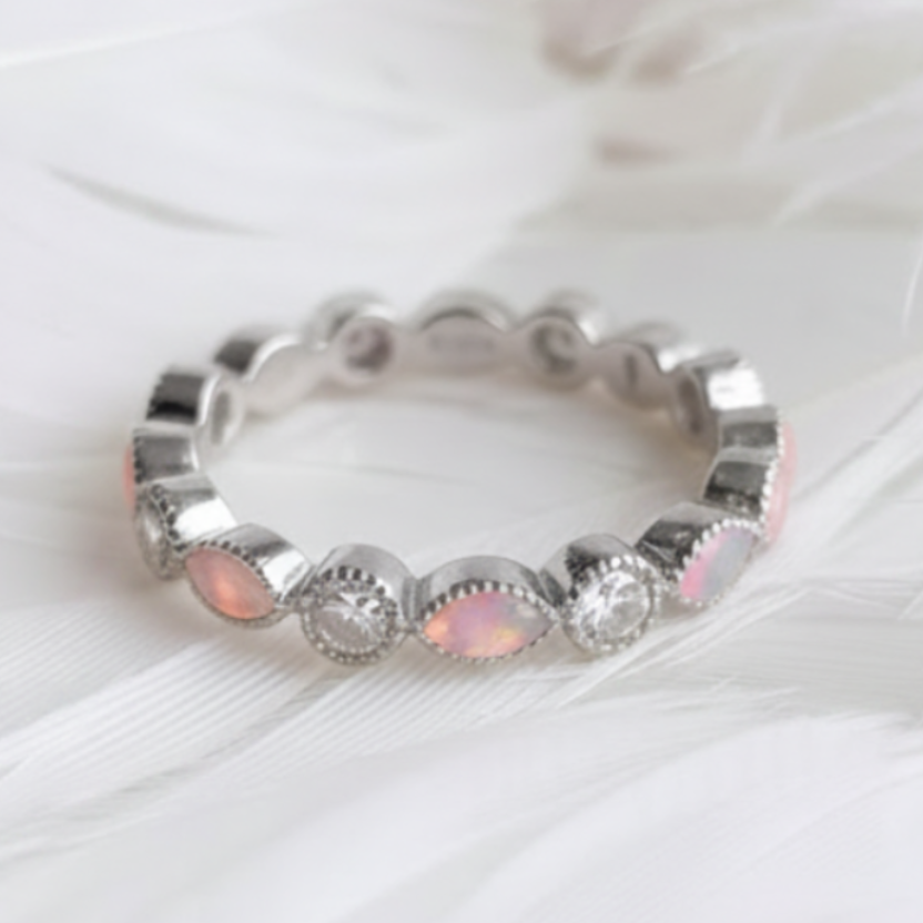 A silver eternity ashes ring featuring pink opal ashes stones and clear round cubic zirconia stones, displayed on a soft white feather background.