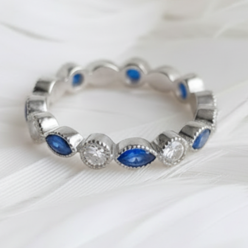 A silver ashes ring featuring sapphire marquis ashes stones and clear round  cubic zirconia stones, displayed on a soft white feather background.