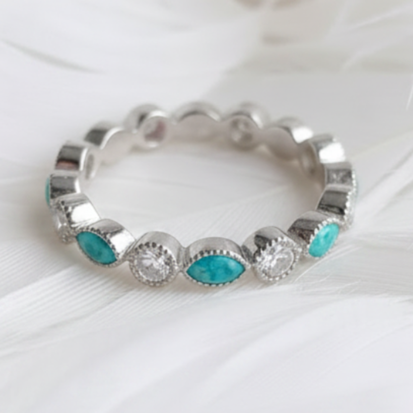 A silver eternity ashes ring featuring marquis turquoise ashes stones, displayed on a soft white feather background.