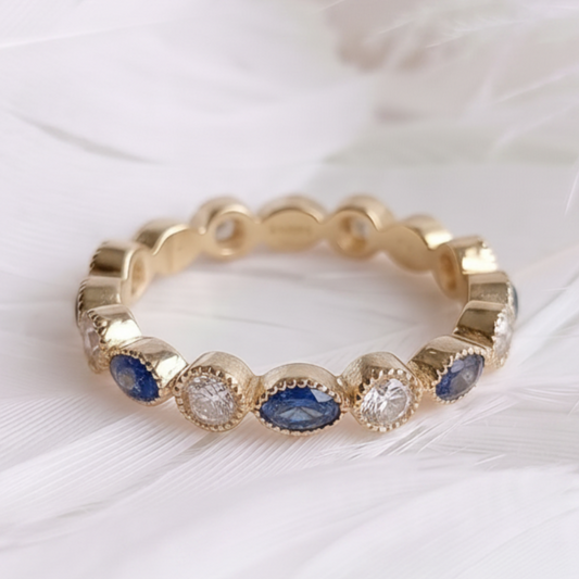 A 14ct 18ct gold ashes eternity ring featuring marquis sapphire ashes stone and genuine diamonds, displayed on a soft white feather background.