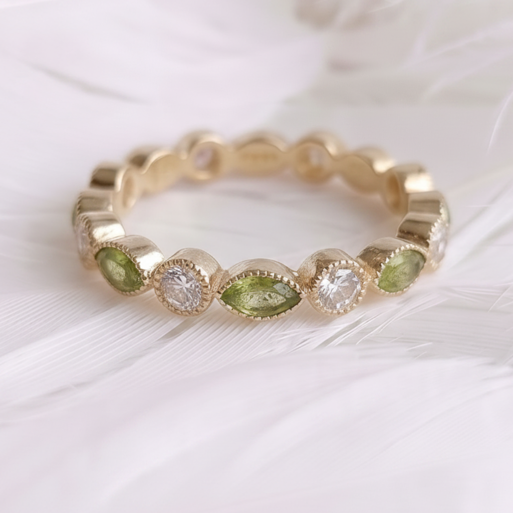 A 14ct / 18ct gold ashes eternity ring featuring marquis peridot ashes stones and genuine d round clear stones, displayed on a soft white feather background.