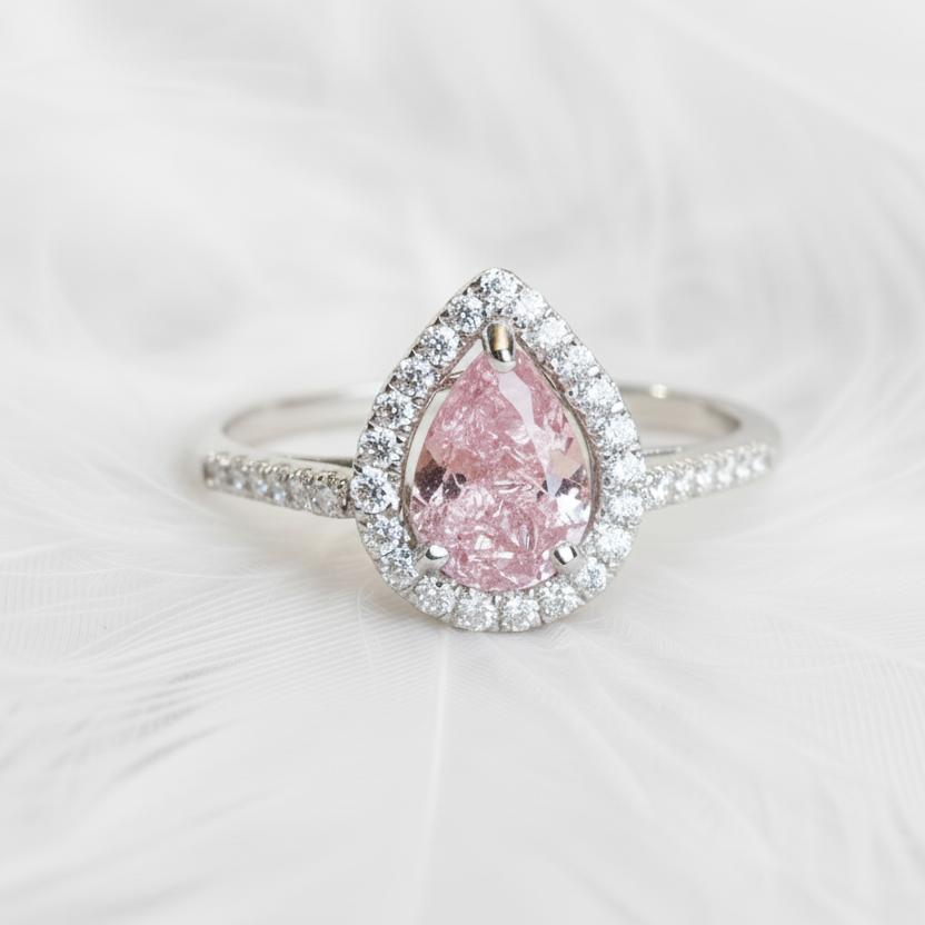 pear shaped ashes memorial ring with halo and stones on shoulder.  Set with a pink memorial stone on a background of ashes