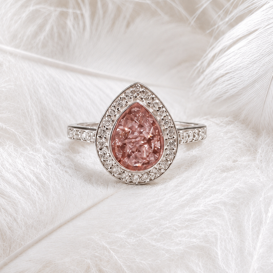 A teardrop-shaped ashes memorial ring with pear centre stone and halo of cubic zirconia. sterling silver band resting on a soft white feathers