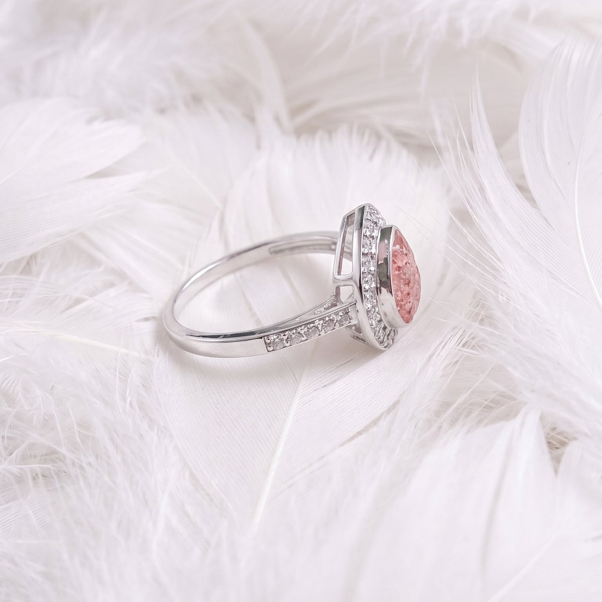 A silver ashes memorial ring with a teardrop gemstone and cubic zirconia side view resting on a bed of white feathers.
