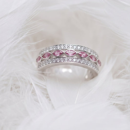 A silver wide band memorial ring with two rows of cubic zirconias and marquise ashes stones in pink, resting on a bed of soft white feathers.